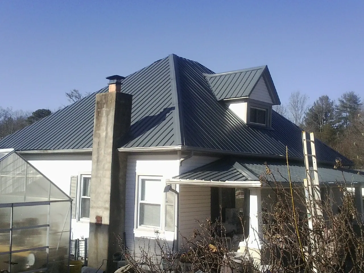 Dark blue standing seam metal roof on a white farmhouse with dormer — Slate & Tile Roof Repair by Roofing Brothers in New Baltimore