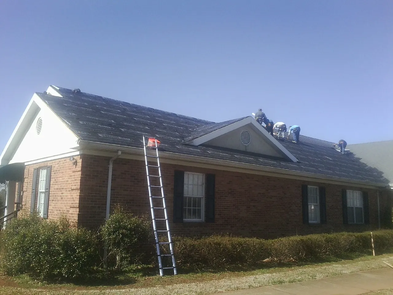 Crew tearing shingles off a brick ranch roof with a ladder set — Metal Roof Repair work by our crew in New Baltimore