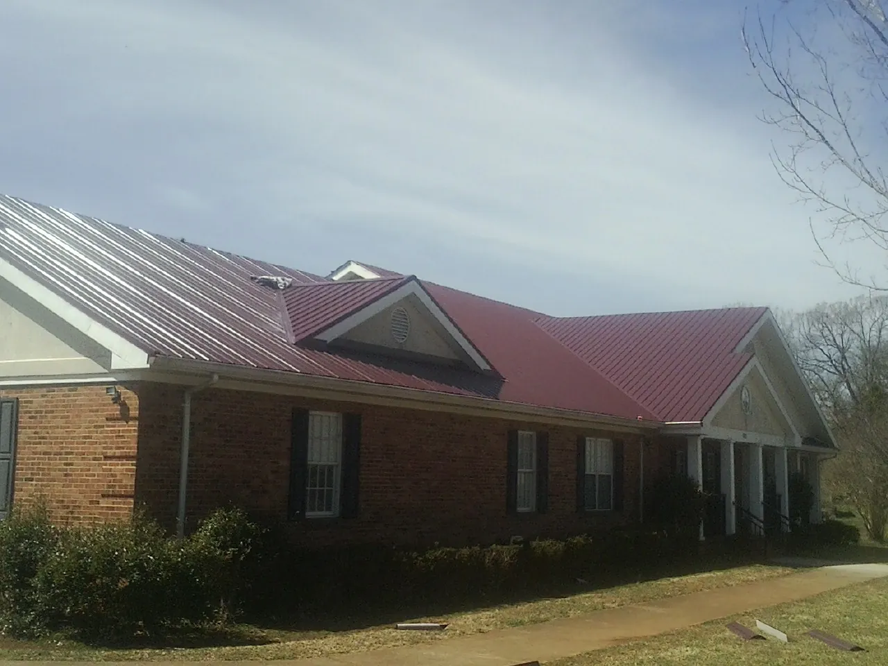 Red metal roof with gabled entries on a long brick building, from a Hail Damage Roof Repair job in New Baltimore