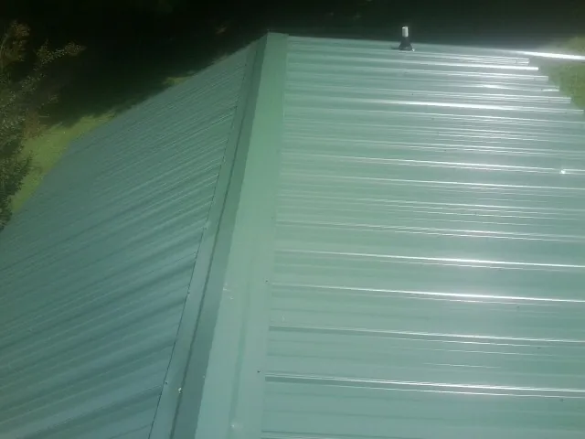 New green metal panels meeting at the ridge of a roof — Flat Roof Repair work by our crew in New Baltimore