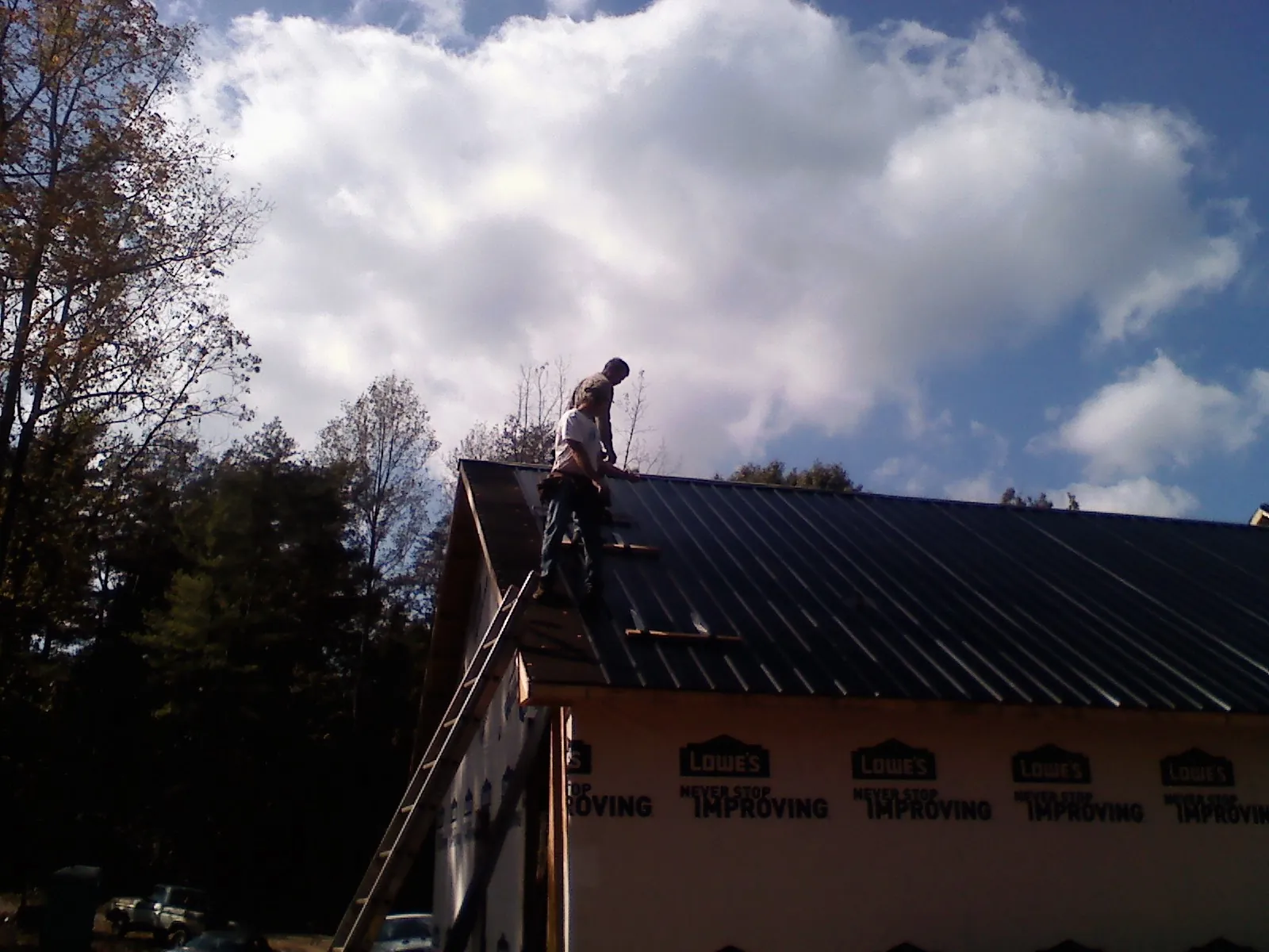 Roofer fastening dark metal panels high against a cloudy sky, from a Roof Inspection job in New Baltimore