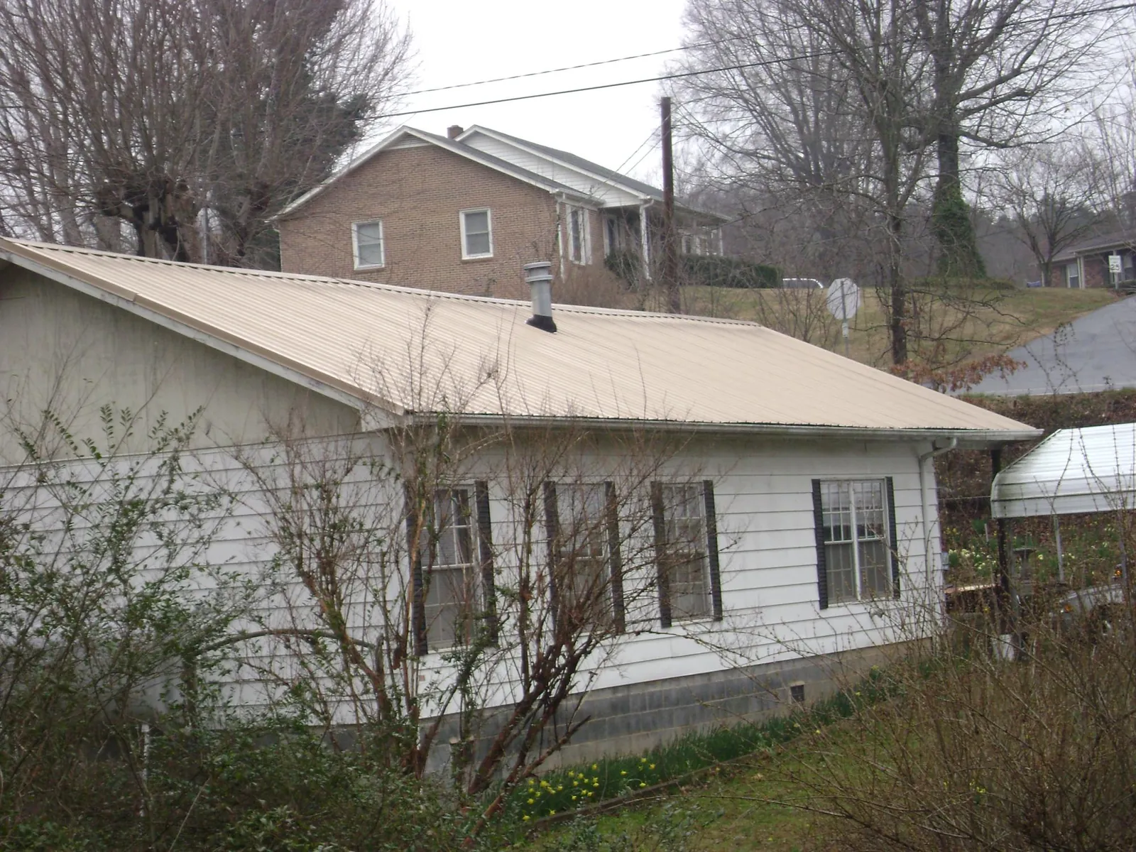 Tan metal roof on a white sided house set into a hillside — Commercial Roofing by Roofing Brothers in New Baltimore