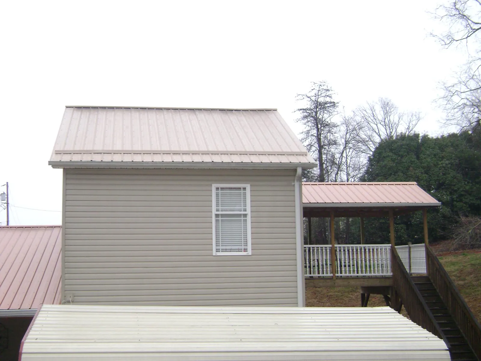 Tan metal roofs on a two story addition and attached porch, from a Roof Replacement job in New Baltimore